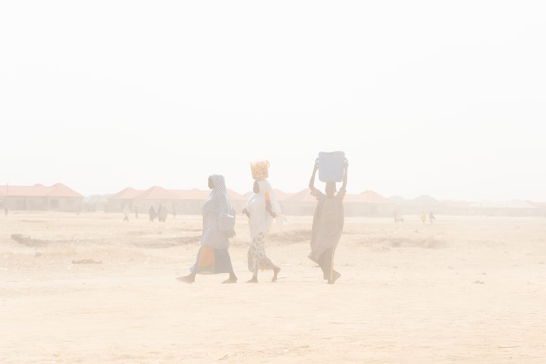 Three persons walk through a sand storm in the Bakassi Camp for internally displaced persons of Maiduguri, north-eastern Nigeria, in December 2018.