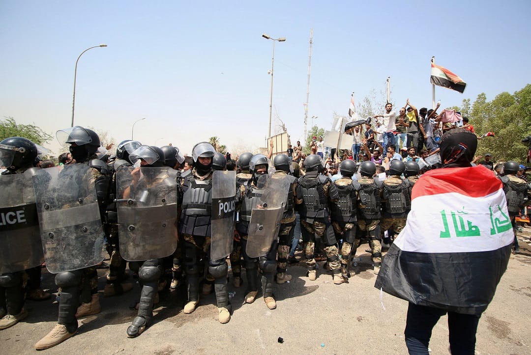 A protester wears an Iraqi flag in front of security forces during a protest near the main provincial government building in Basra, Iraq 15 July, 2018.